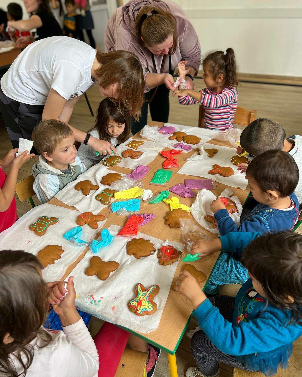 Fotografia ilustracyjna z małymi dziećmi przy stole lepiącymi ciastka