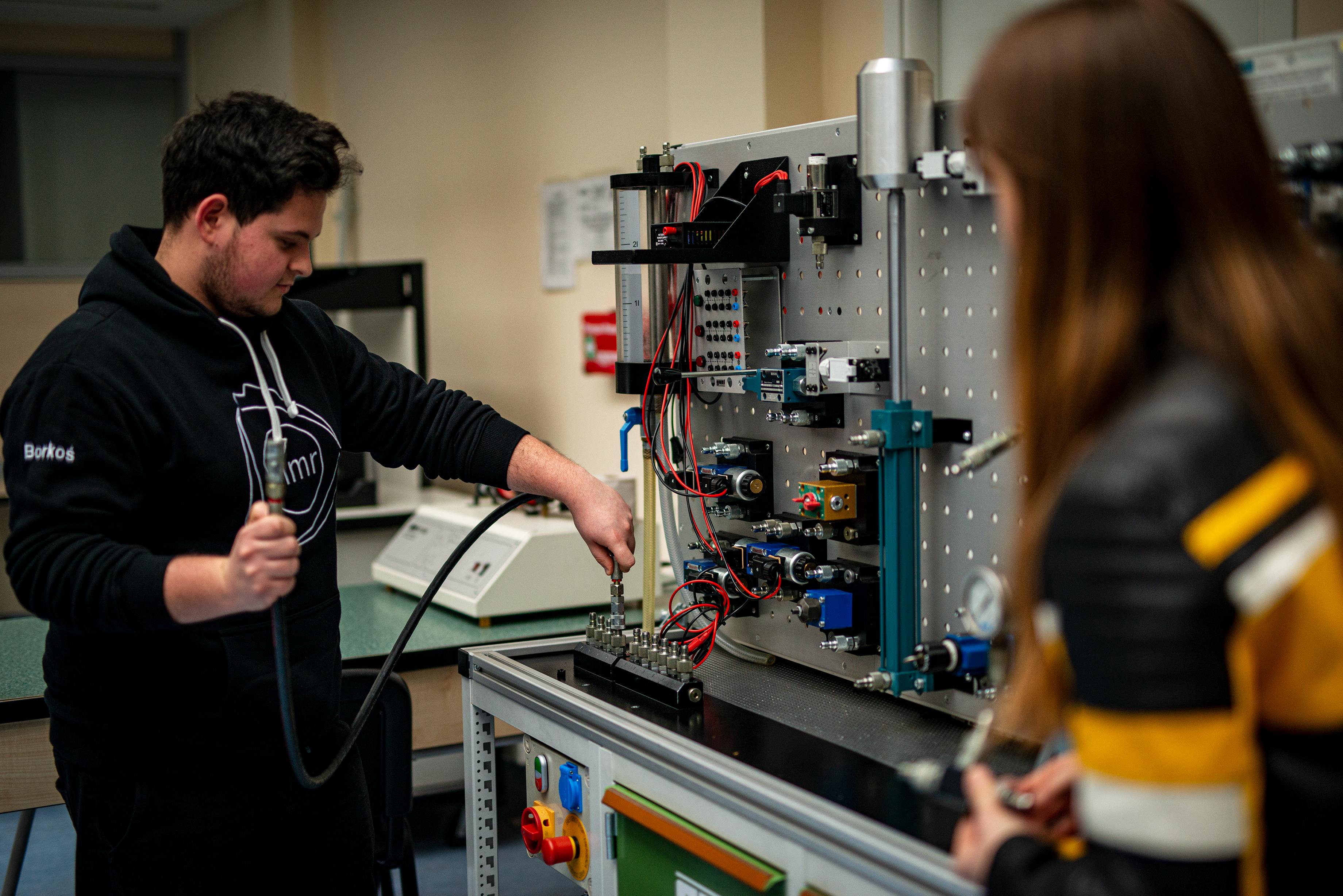 Student łączący przewody hydrauliczne na stanowisku laboratoryjnym.