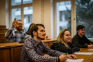 Grupa uśmiechniętych studentów w ławkach sali wykładowej.