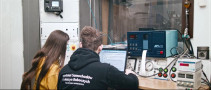 Sylwetki dwóch osób siedzących przy stole z aparaturą elektroniczną