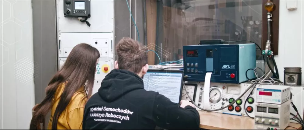 Sylwetki dwóch osób siedzących przy stole z aparaturą elektroniczną